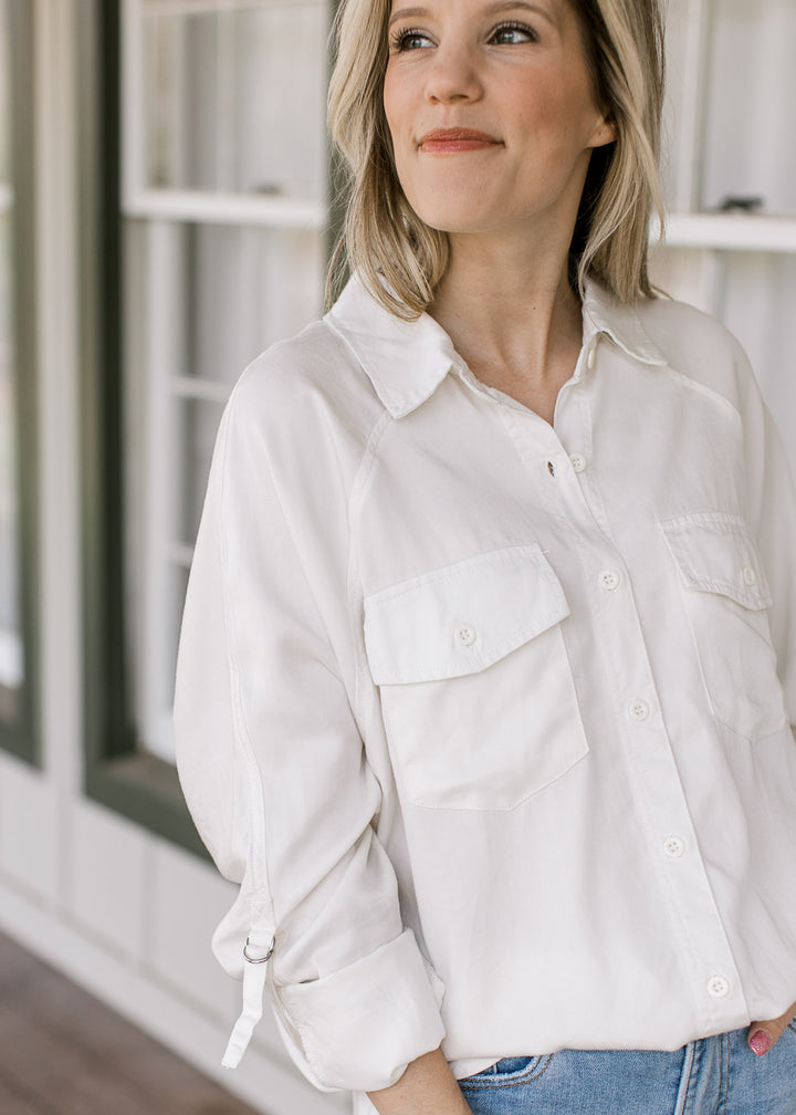 Close up of patch pockets and 3/4 sleeve with clasp on a model wearing a button up cream top.