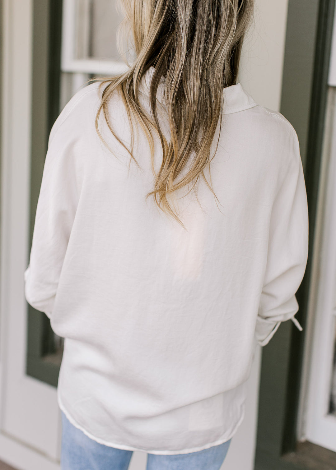 Back view of Model wearing a cream button down top with long sleeves and 3/4 clasp.