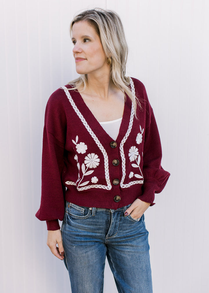 Model wearing a wine v-neck sweater with white embroidery, button front and bubble long sleeves.