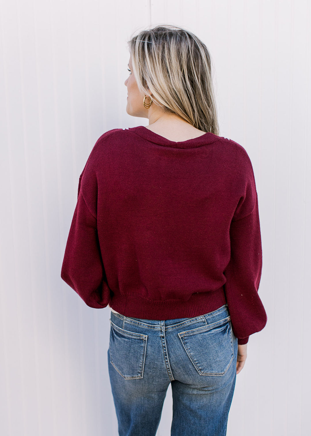 Back view of Model wearing a wine sweater with white embroidery and a cropped fit.