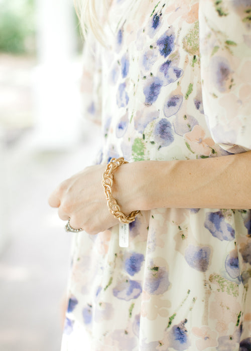 Model wearing an interlocking chain bracelet with a stretchy band and a matte gold color. 