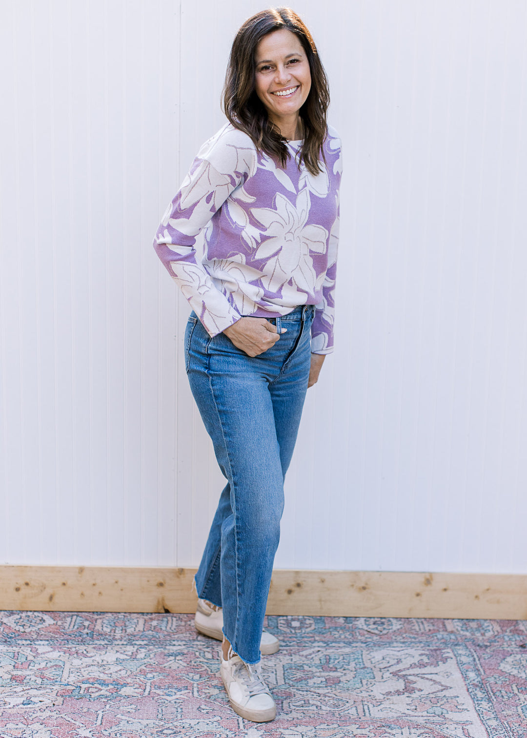 Model wearing a lavender long sleeve sweater with cream flowers and metallic details.