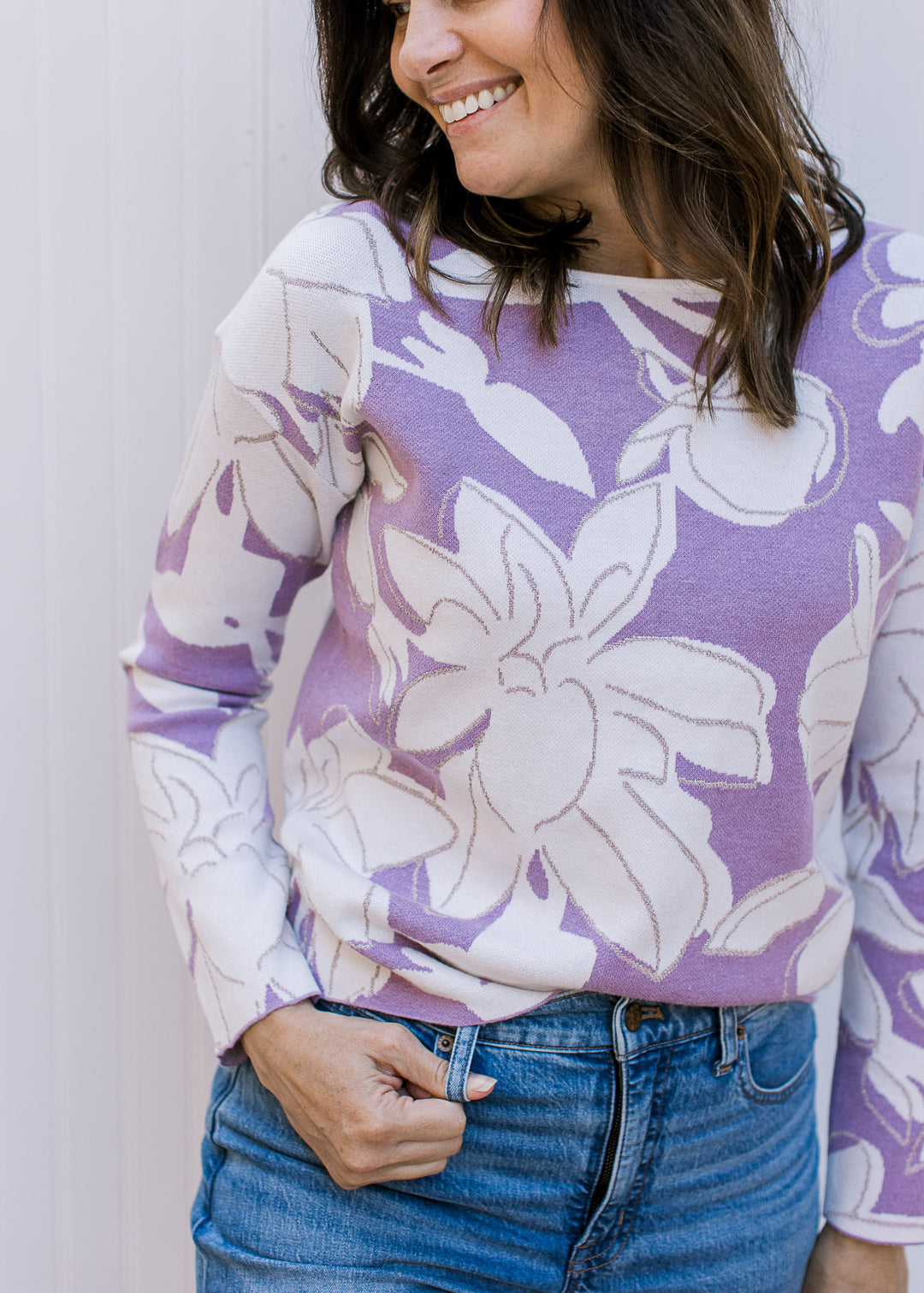 Close up of model wearing a lavender long sleeve sweater with cream flowers and metallic details.