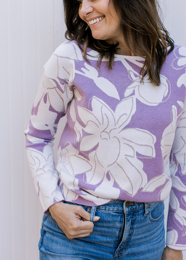 Close up of model wearing a lavender long sleeve sweater with cream flowers and metallic details.