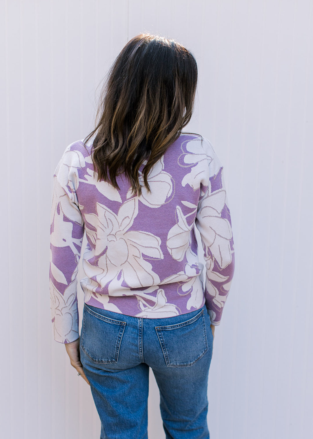 Back view of Model wearing a lavender long sleeve sweater with cream flowers and metallic details.