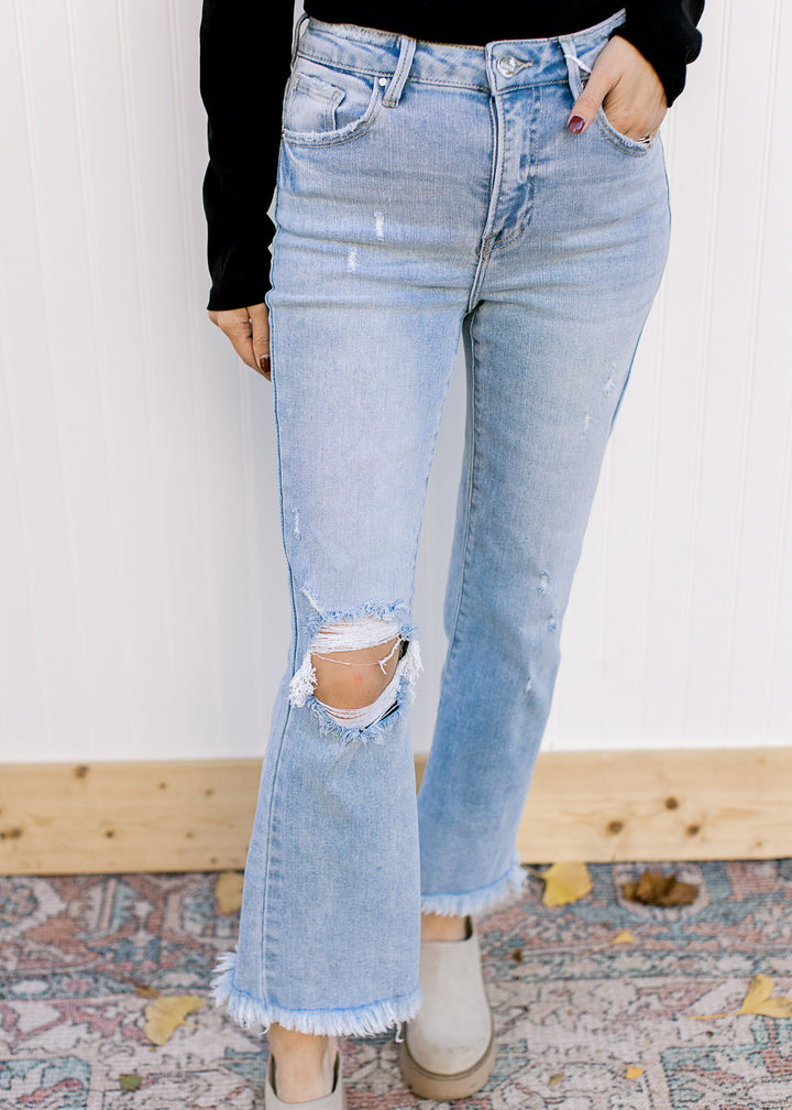 Close up of distressed knee on light wash jeans with a high waist and a frayed cropped hem.