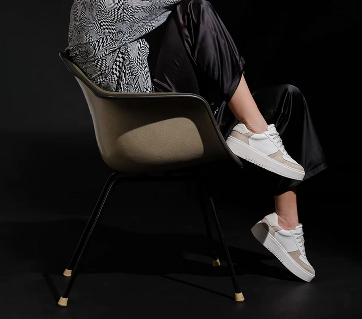 Model sitting wearing a white and taupe shoe with a platform sole and laces.