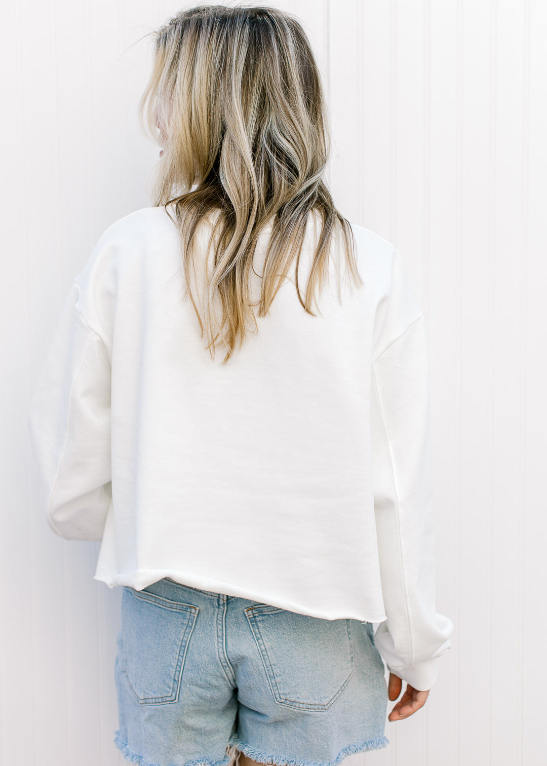 Back view of Model wearing a slightly cropped white sweatshirt with a fabric USA patch.