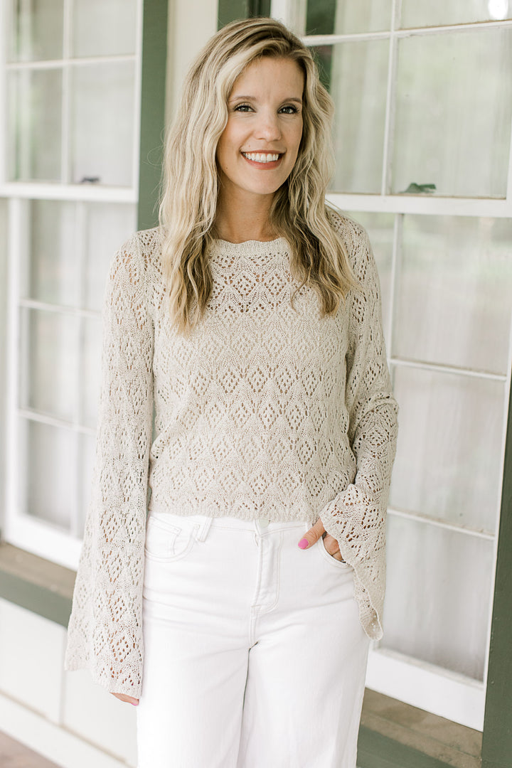 Model wearing a cream loose knit sweater with scallop detail at the neck, cuff and hem.