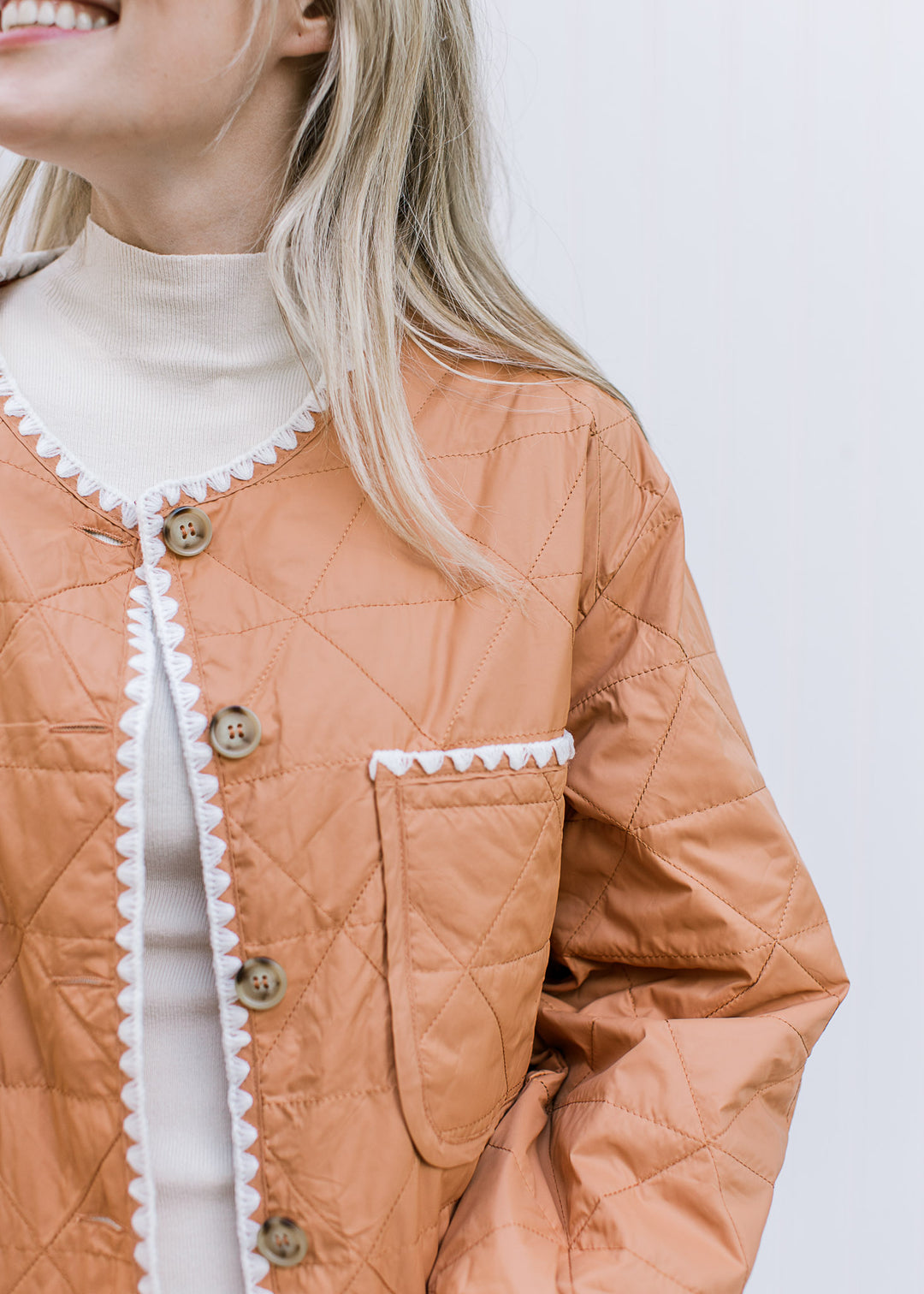 Close up of pockets and button up on an amber colored quilt jacket with long sleeves.