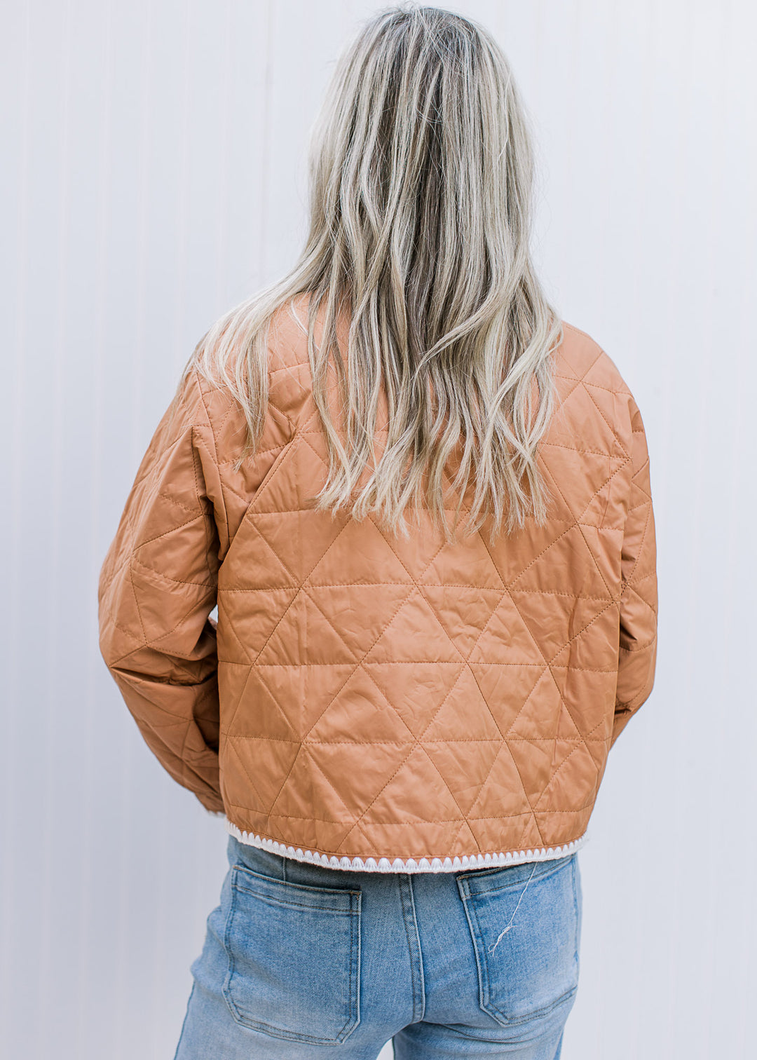 Back view of Model wearing an amber colored quilt jacket with cream embroidery and long sleeves.