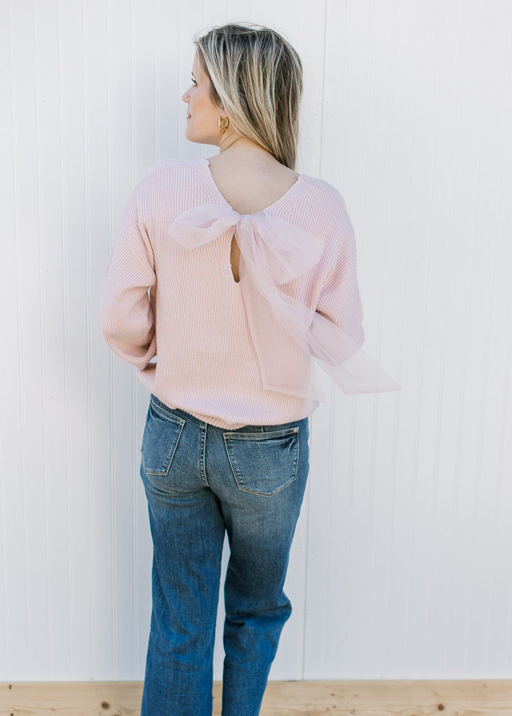 Back view of model wearing a blush sweater with a mesh bow and ribbed material.