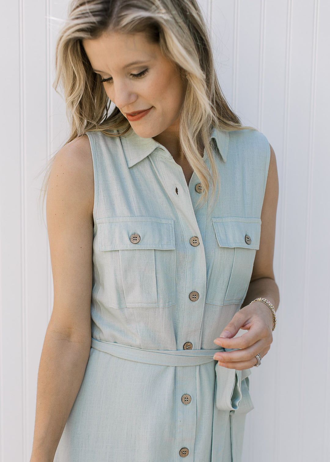 Close up of button front, patch pockets, tie waist and a collar on a soft basil sleeveless dress.