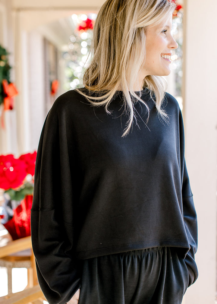 Model wearing a black sweatshirt with long sleeves, round neck and a slightly cropped fit.