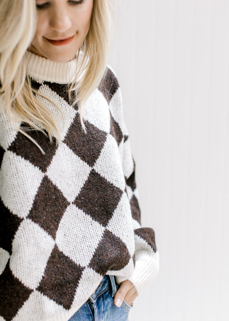 Model wearing a brown and white diamond pattern sweater with a round ribbed neck and long sleeves. 