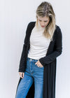Model wearing jeans and a white top with a black long sleeve cardigan with a duster length. 