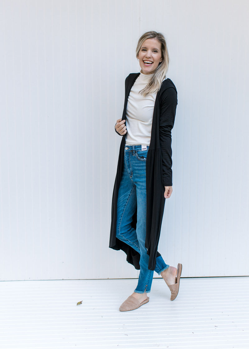 Model wearing jeans a white top and mules with a black long sleeve cardigan with a duster length. 