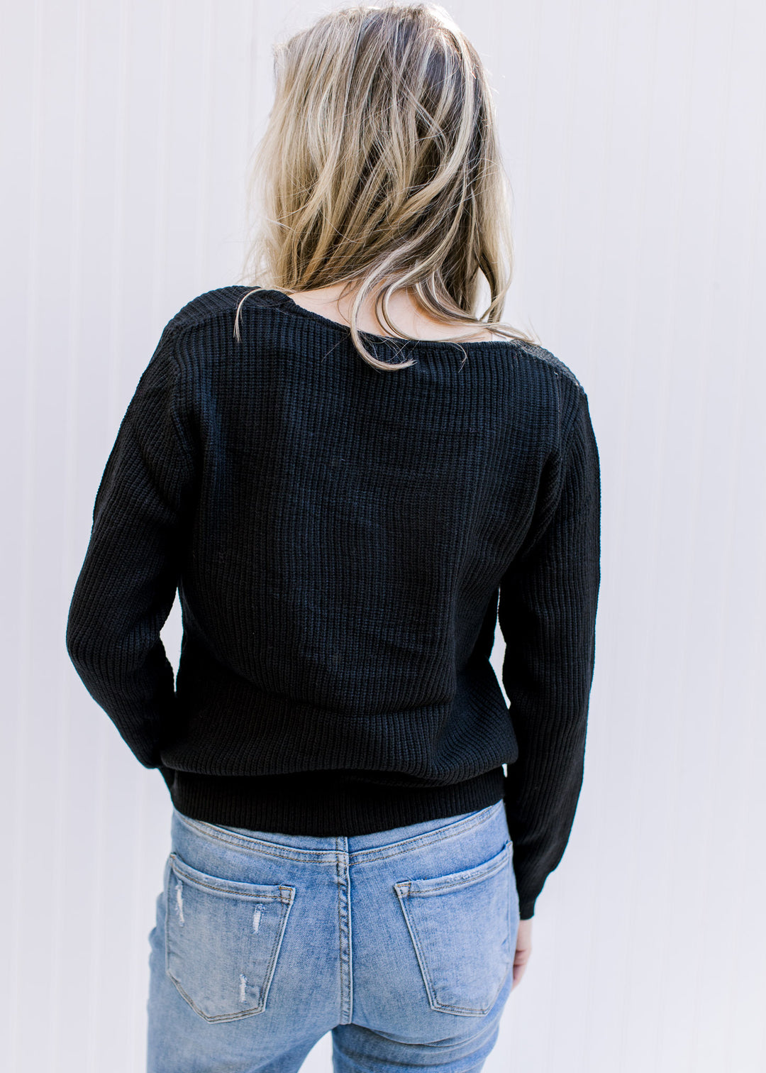Back view of Model wearing a lightweight black ribbed top with long sleeves and a round neckline.