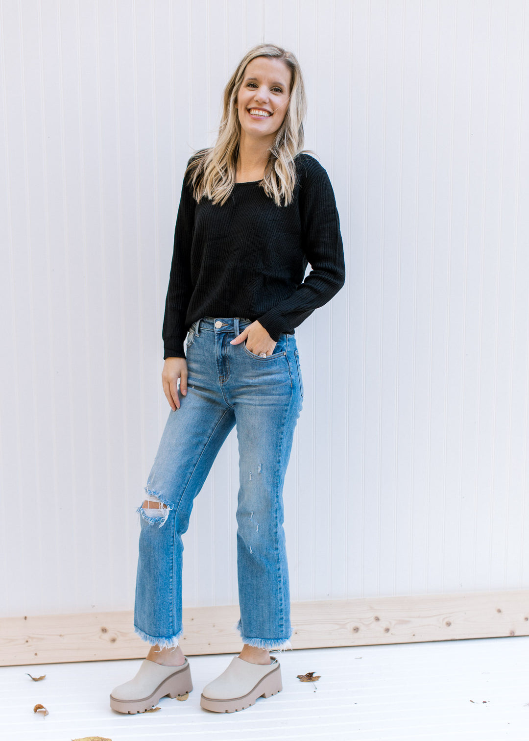 Model wearing jeans and a lightweight black ribbed top with long sleeves and a round neckline.