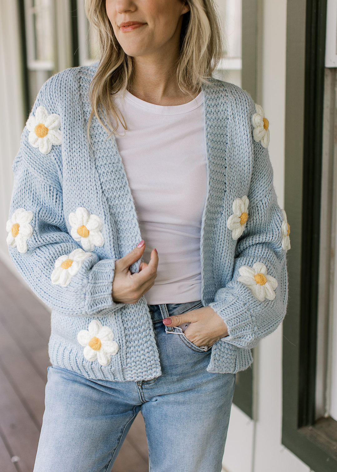 Model wearing a knit cornflower blue cardigan with white daisies and long sleeves.