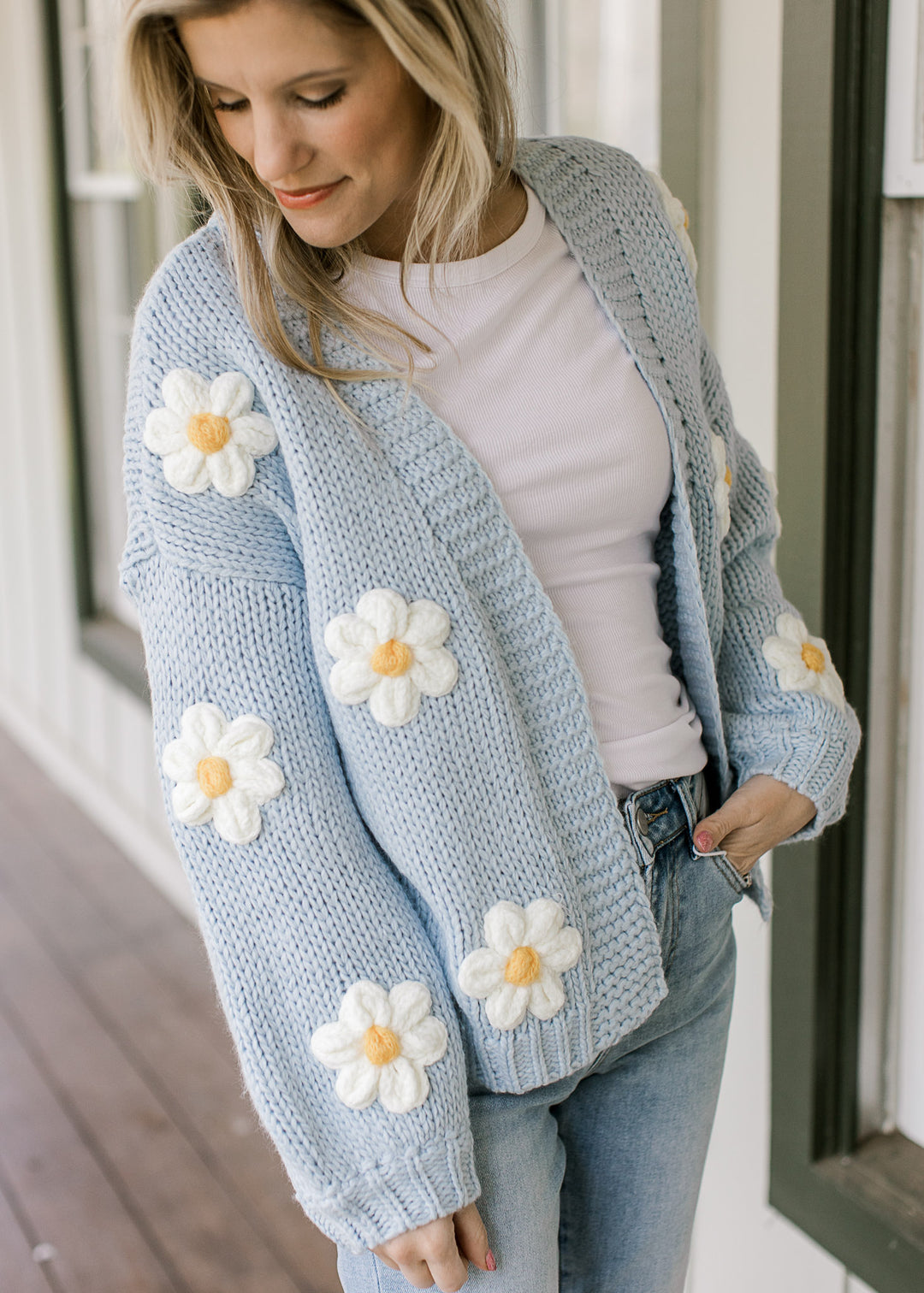 Model wearing a white top with a knit cornflower blue cardigan with white daisies.