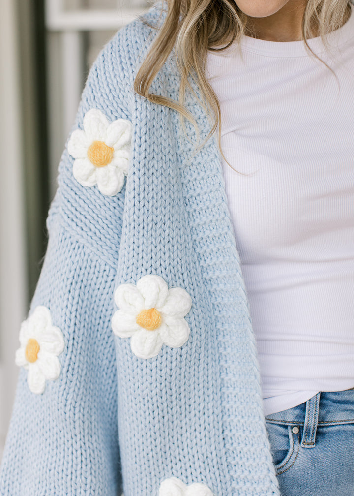 Close up of white daisies on a cornflower blue cardigan with open front and long sleeves.
