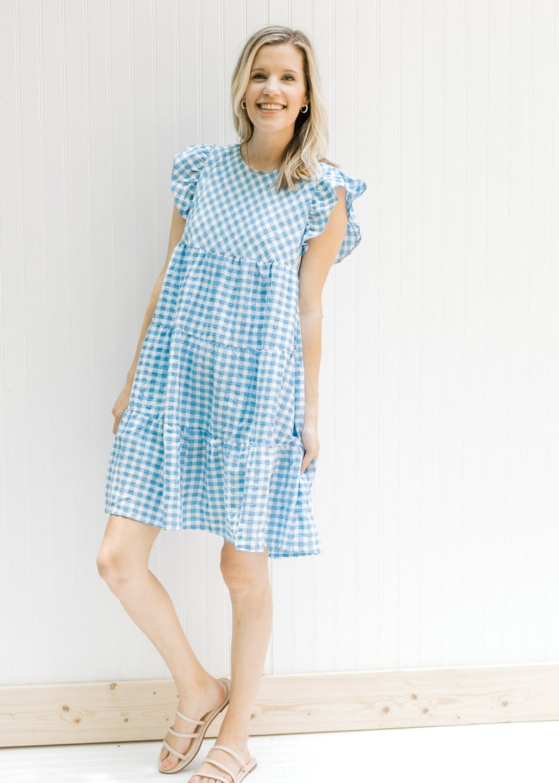 Model wearing sandals with a blue and white tiered gingham dress with ruffle cuff sleeves. 