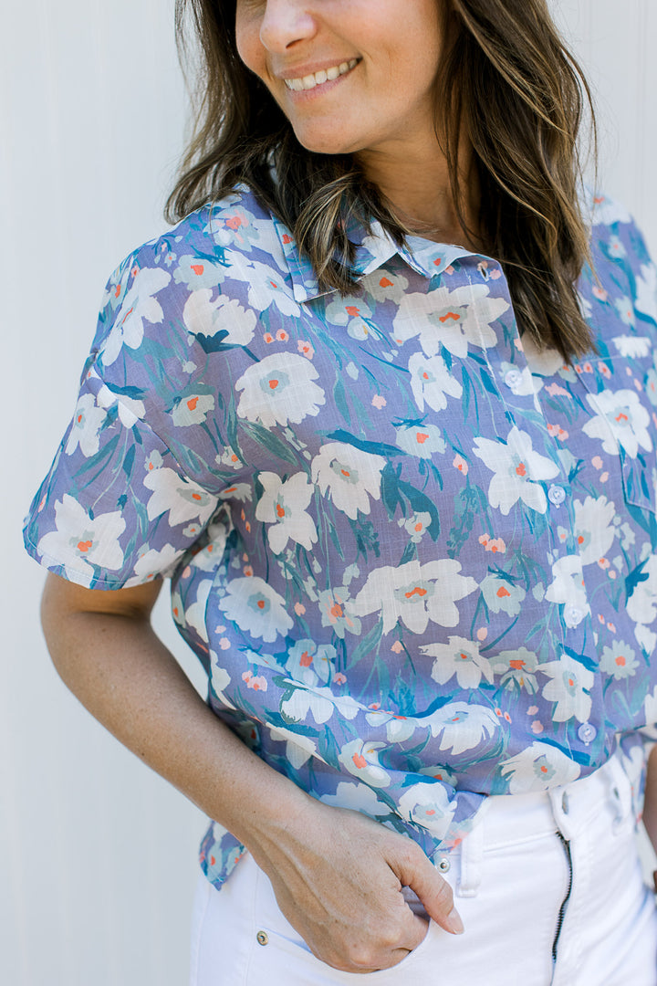 Close up of button front on a lavender short sleeve top with flowers and a collar.