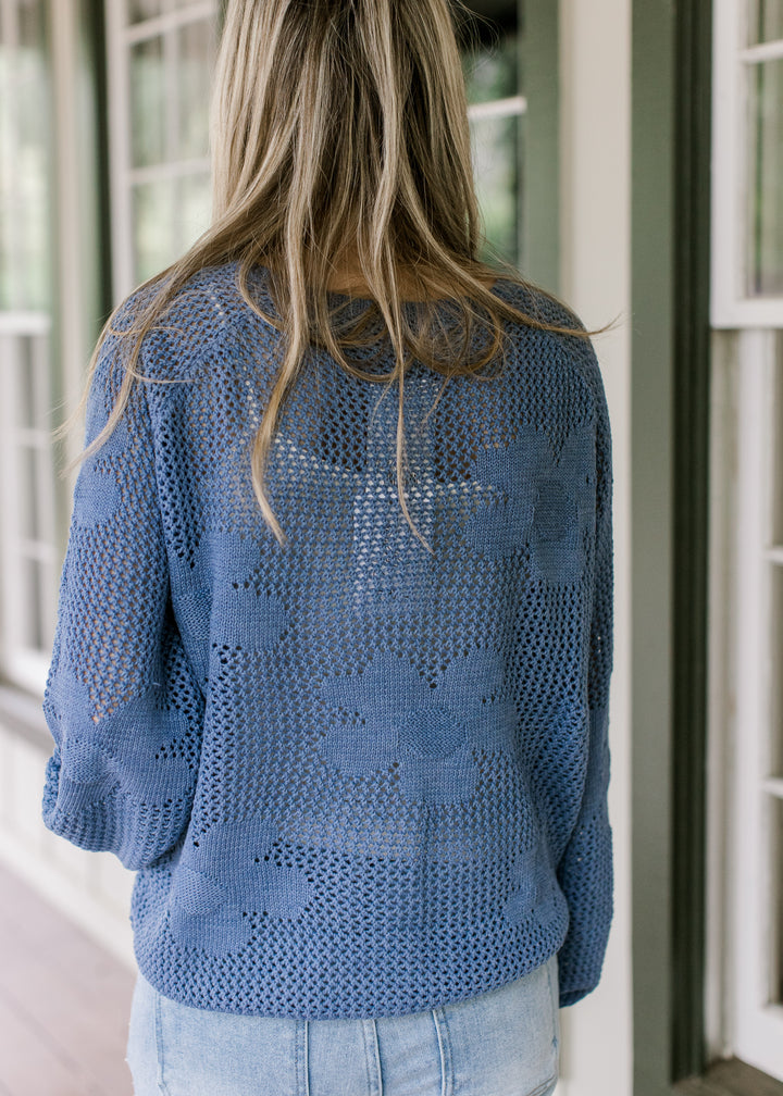 Back view of Model wearing a blue open weave sweater with stitched flowers and bubble long sleeves.