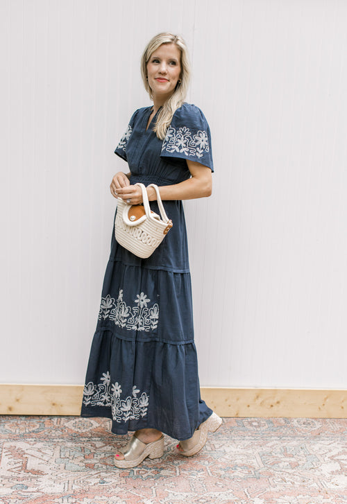 Model wearing wedges with a blue maxi with white stitched flowers, v-neck and short sleeves.
