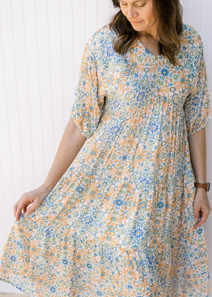 Model wearing a flowy cream midi with blue, green and orange flowers and 3/4 sleeves.