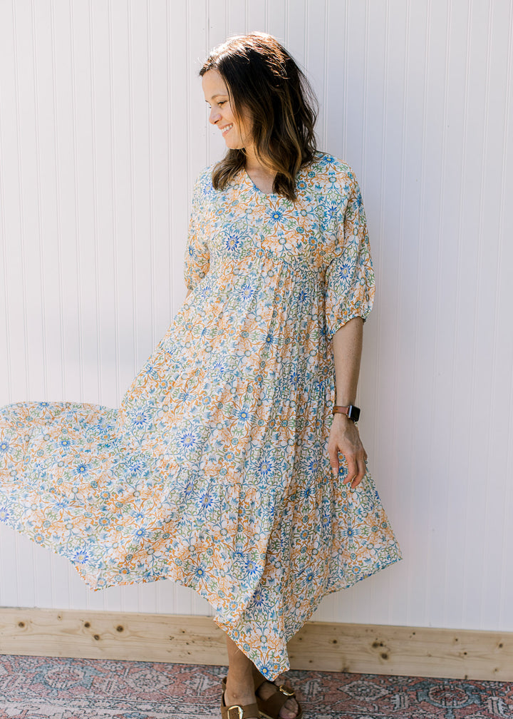 Model wearing sandals with a cream midi with blue, green and orange flowers and 3/4 sleeves.
