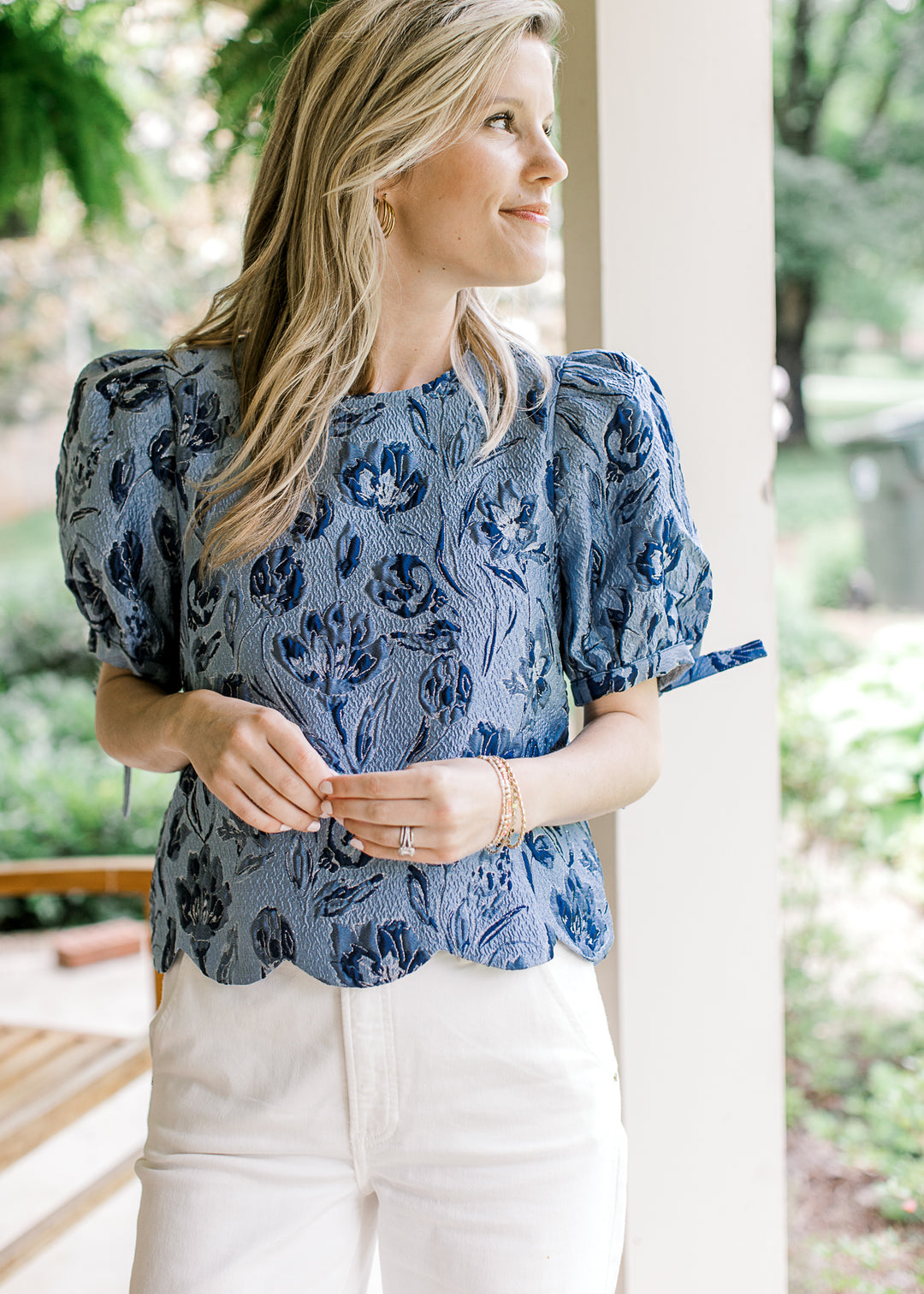 Model wearing a soft blue top with navy textured flowers and bubble short sleeves with a tie.
