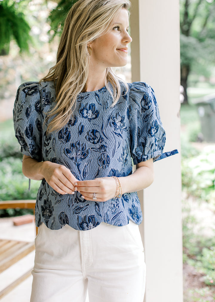 Model wearing a soft blue top with navy textured flowers and bubble short sleeves with a tie.