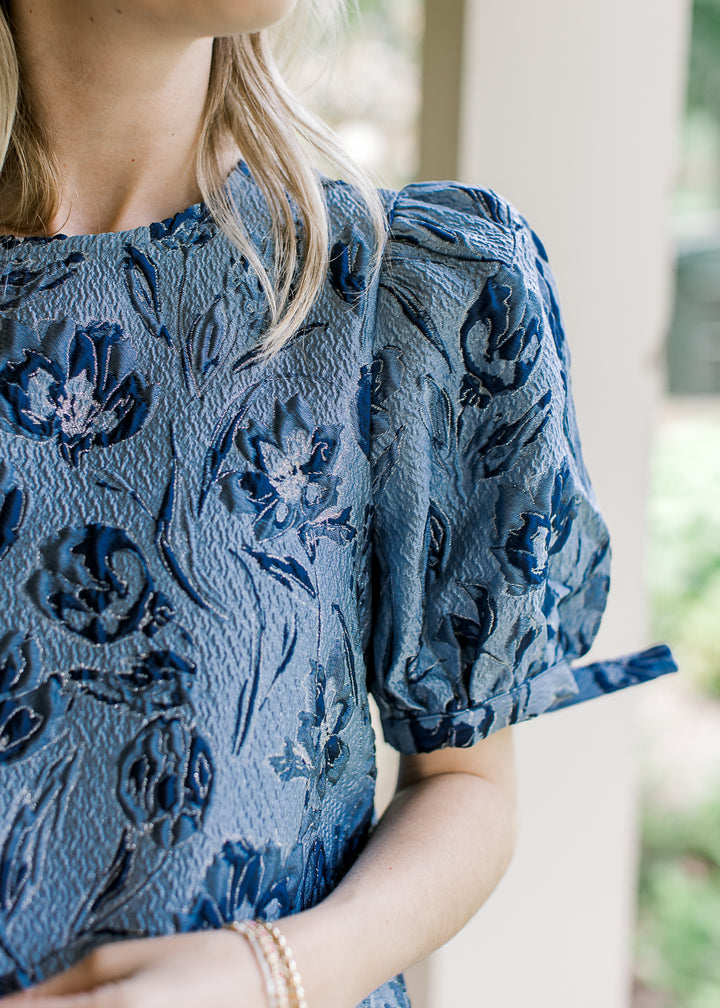 Close up of navy textured flowers on a light blue top with bubble short sleeves with a tie.