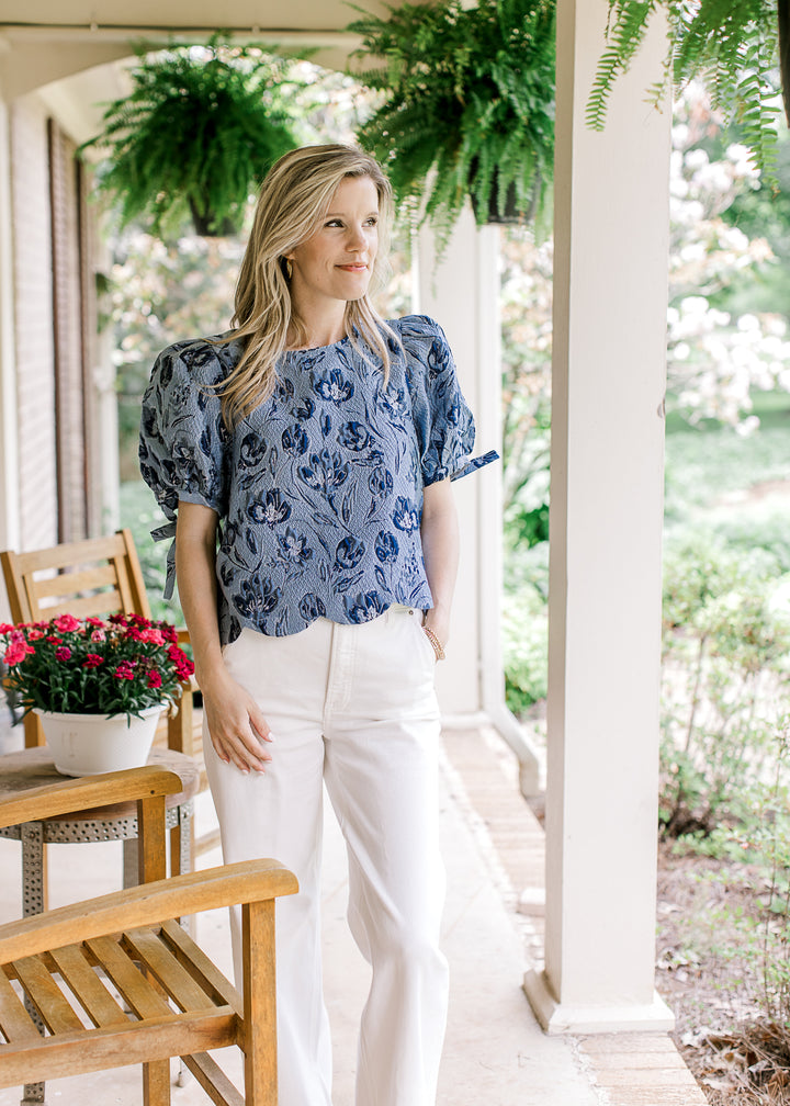 Model wearing a soft blue top with navy textured flowers, bubble short sleeves and scalloped hem.