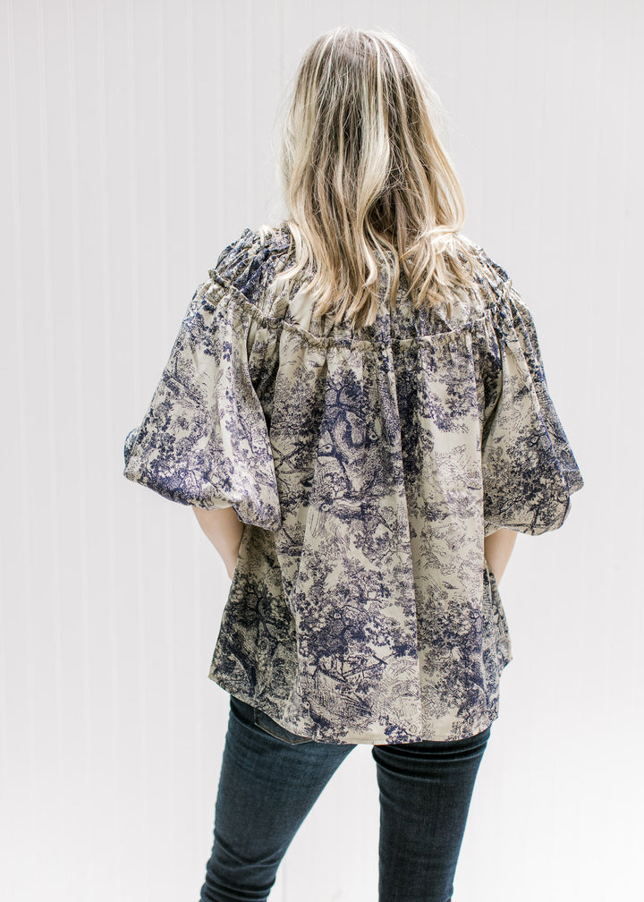 Back view of Model wearing a tan top with navy toile print, short sleeves and ruched neck detail.