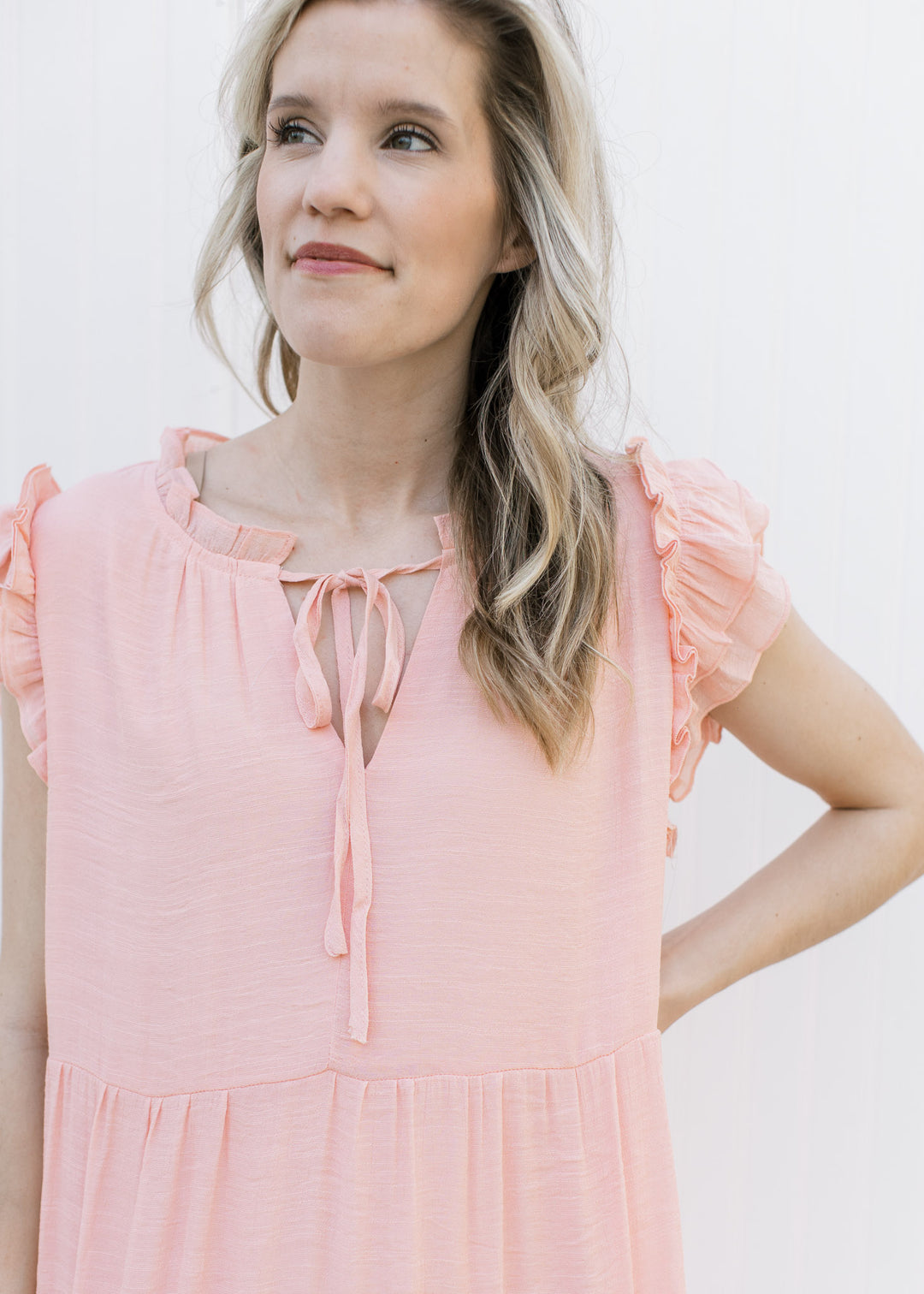 Close up of ruffled cap sleeves and v-neck with a tie on a blush midi with a tiered skirt.