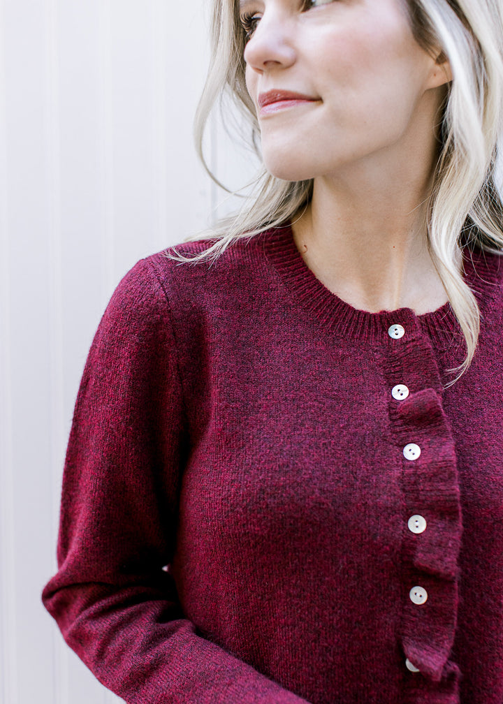 Model wearing a burgundy knit sweater with pearl buttons and ruffle at placket, hem, and cuffs.