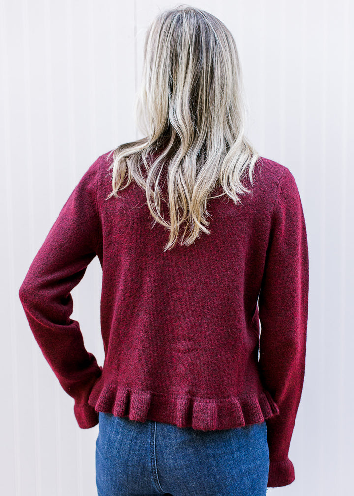 Back view of Model wearing a long sleeve burgundy knit sweater with a ruffle at hem and cuffs.