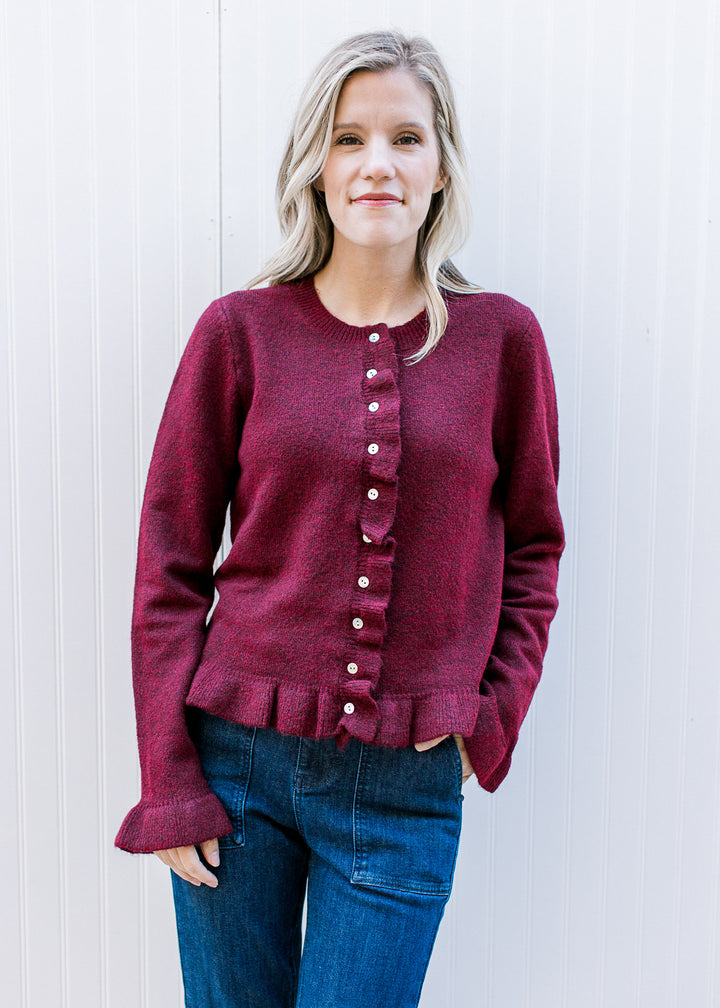 Model wearing a burgundy long sleeve sweater with pearl buttons, round neck and ruffle detail.