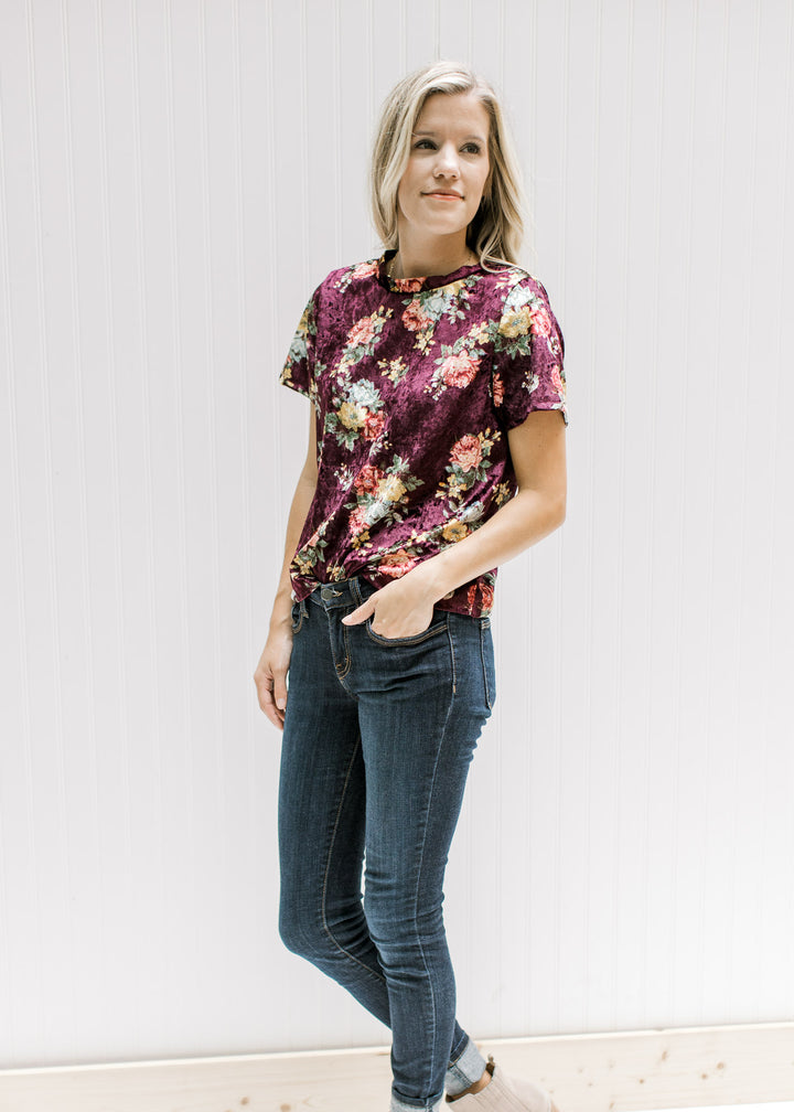 Model wearing jeans with a burgundy velvet top with a yellow, pink and blue floral pattern.