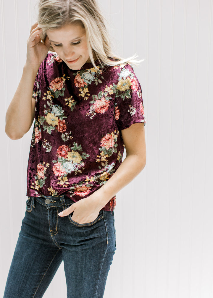 Model wearing a burgundy velvet top with a yellow, pink and blue floral pattern and jeans.
