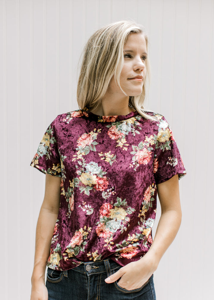 Model wearing a burgundy velvet top with a yellow, pink and blue floral pattern and short sleeves.