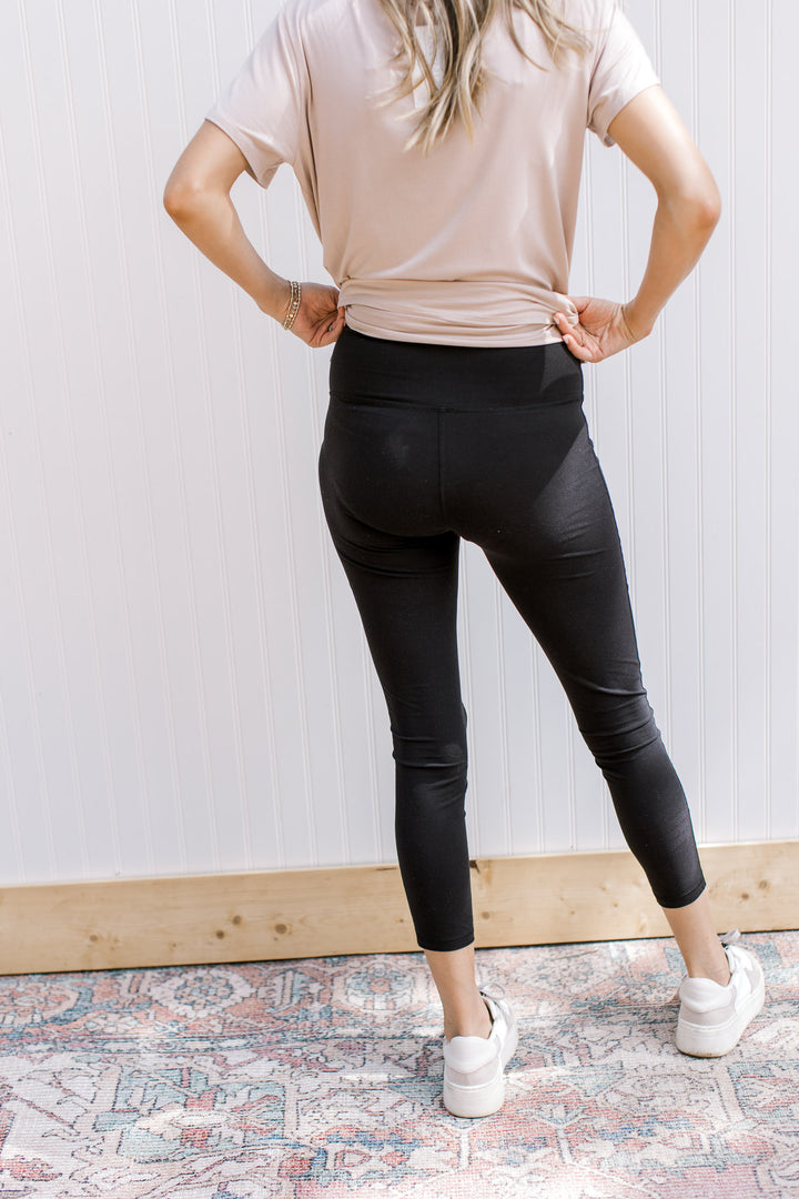 Back view of Model wearing black cropped leggings with an elastic waistband and ultra soft material.