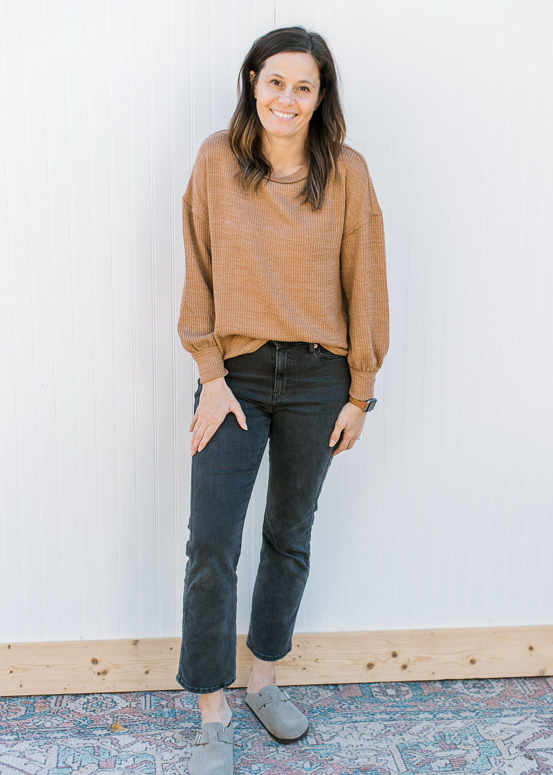 Model wearing black pants, clogs and a ribbed camel top with long sleeves and a round neck.