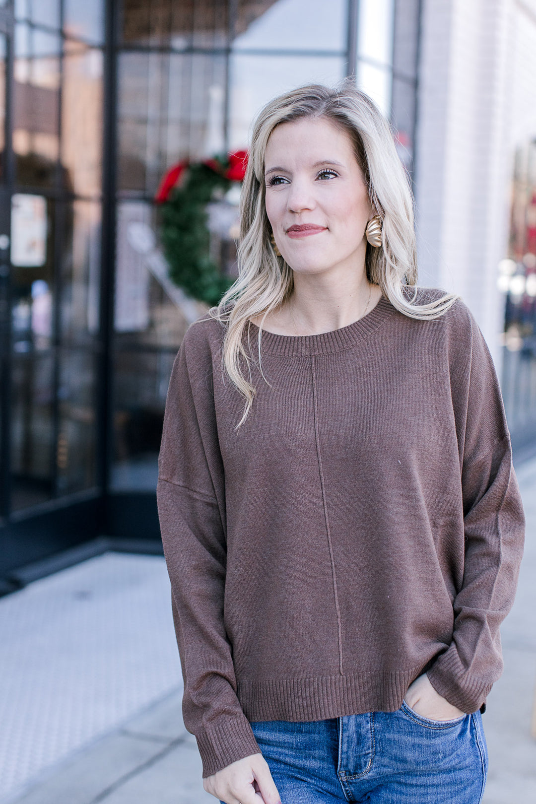 Model wearing a brown sweater with long sleeves, round neck and ribbed neck, hem and cuff.