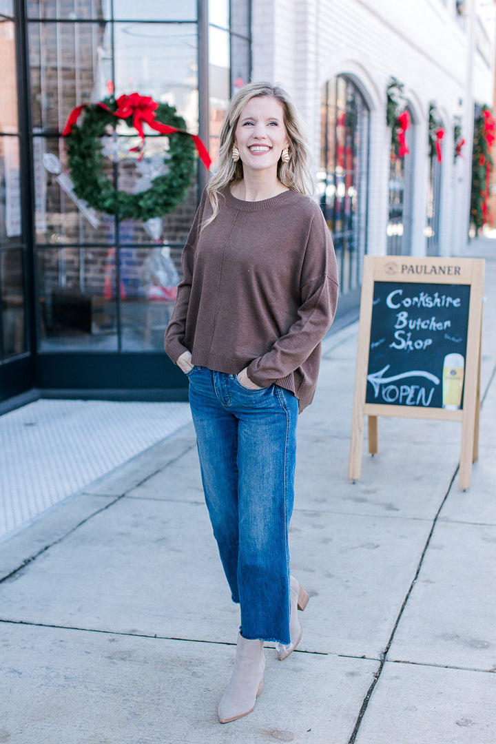 Model wearing jeans, booties and a brown sweater with long sleeves and a round neck.