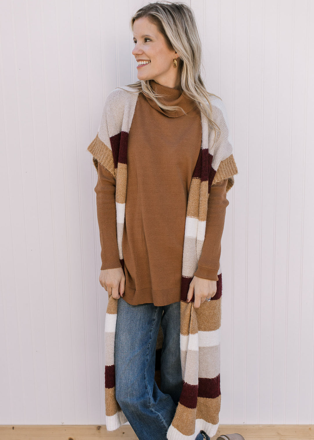 Model wearing a rust top and colorblock knit duster with cream, camel and  maroon stripes