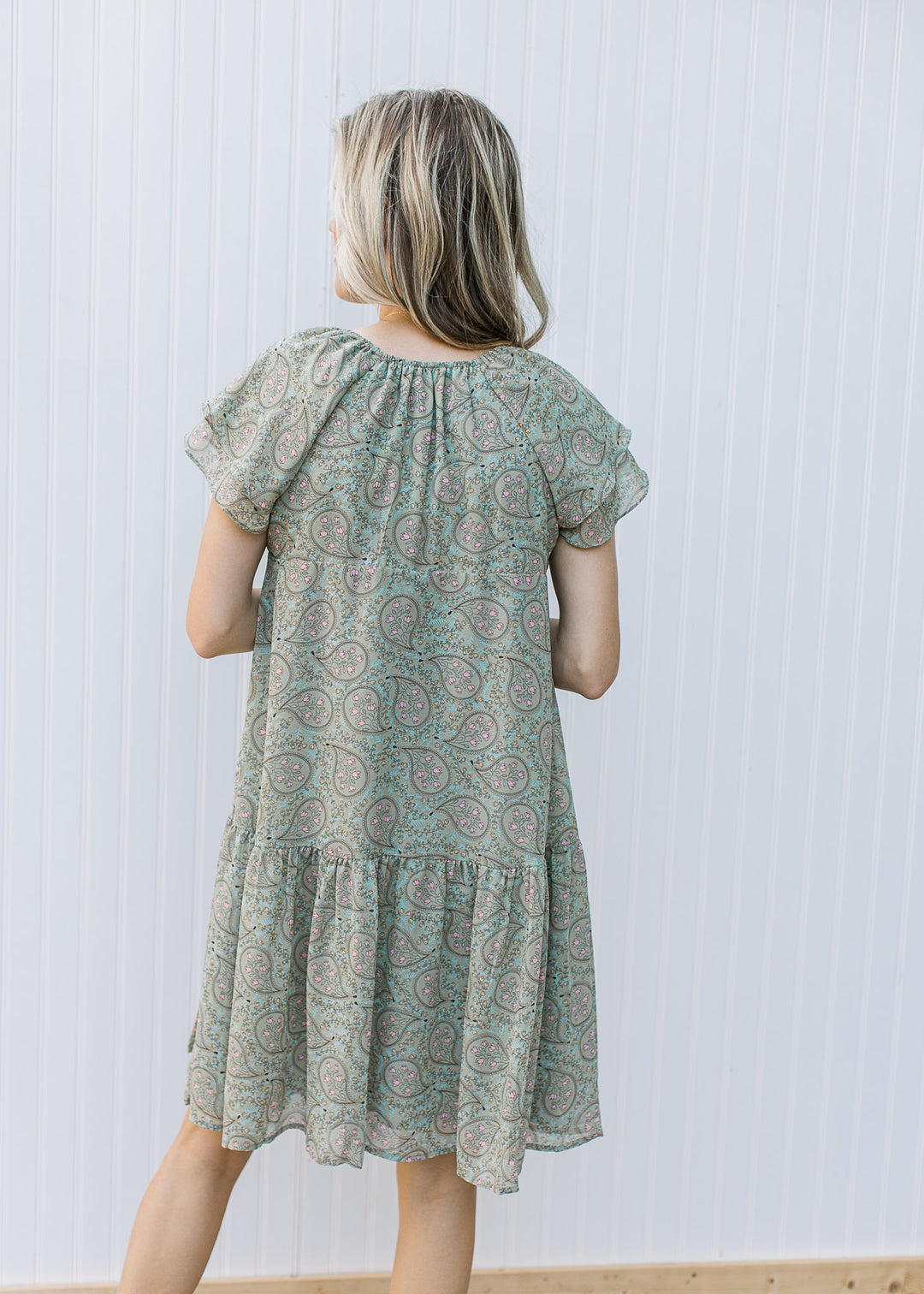 Back view of Model wearing a sage dress with paisley design, layered short sleeves and v-neck.